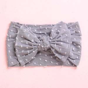 Detail of grey baby nylon headband with white polka dots and oversized bow on pink background