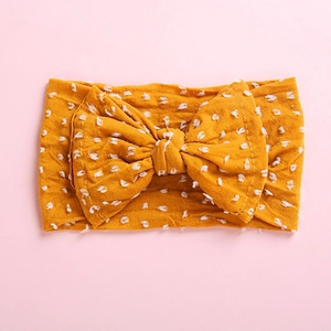 Detailed close-up of ginger yellow bow headband with white plush polka dots on pink background