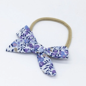 Detail of floral cotton bow baby headband with purple and blue blossoms on a nude nylon strap