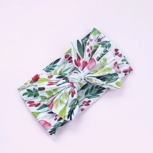 Détail d'un bandeau bébé à imprimé floral rouge avec nœud fait main sur fond rose pâle