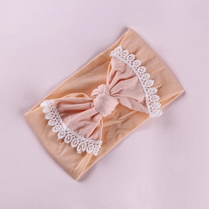 Detail of baby nylon headband with peach bow and white lace embroidery edging