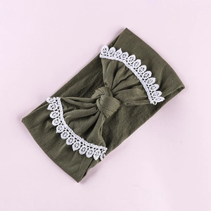 Close-up of olive green baby headband with white lace trim and bow on pink background