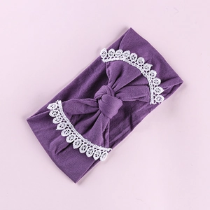 Detail of dark purple baby headband featuring large bow and white lace floral trim