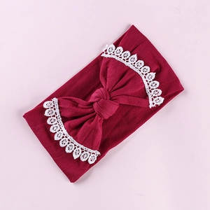 Detailed view of burgundy baby headband with large bow and white lace embroidered edges