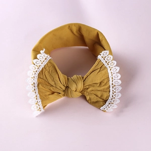 Detailed close-up of mustard yellow baby headband with white lace bow and soft fabric texture