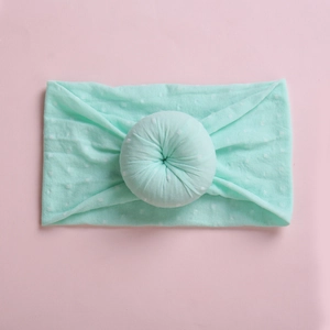 Detail of mint green baby headband with white polka dots and circular pleated knot