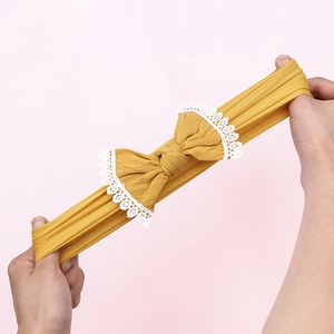 Detail of mustard yellow nylon baby headband with lace bow showing high elastic stretch