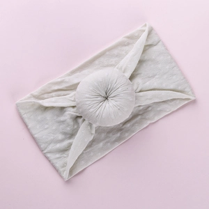 Detail of soft cream knitted baby headband featuring a textured donut knot on pink background