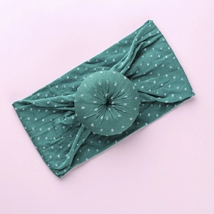 Close-up of dark green donut-style baby headband with white patterns on pink background