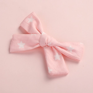 Detail of pink cotton bow hair clip with white star print on a soft pink background
