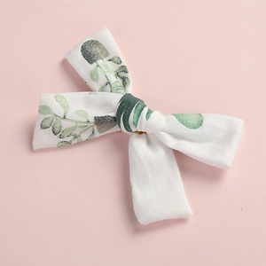 Close-up of a white cotton bow hair clip with fresh green leaf print on pink background