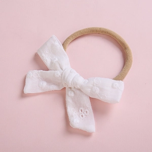 Détail de la broderie en dentelle blanche sur un bandeau doux pour bébé avec nylon