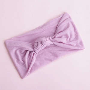 Close-up of violet soft nylon baby headband with classic knot design on pink background