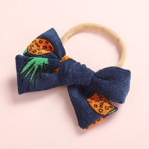 Detail of baby headband with dark blue corduroy bow and orange pineapple print on nylon band