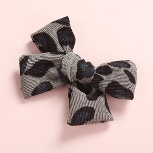 Detailed close-up of grey corduroy bow hair clip with black leopard pattern on pink base