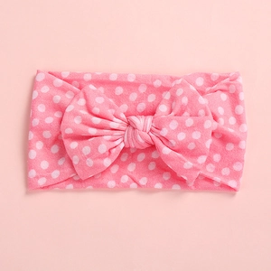 Detailed view of pink baby headband with large polka dot bow in soft elastic fabric