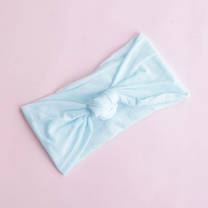 Detail of soft light blue nylon knotted baby headband on a pastel pink background