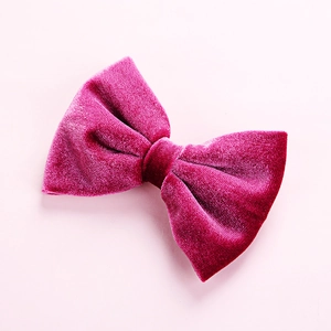 Detailed texture of a magenta velvet bow hair clip for kids on light pink background