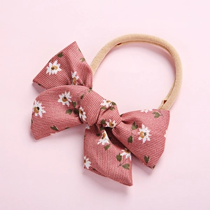 Soft nylon baby headband with a brick-red floral pinwheel bow on a pink background