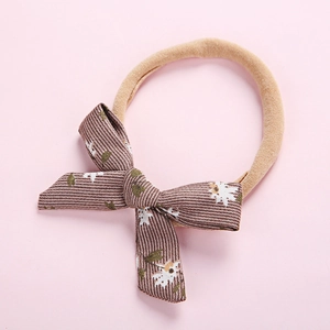 Detail of baby headband featuring brown floral corduroy bow on nude nylon band
