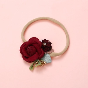 Détail d'un bandeau artisanal avec rose en tissu rouge foncé et bande en nylon élastique