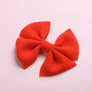 Detailed close-up of an orange waffle textured fabric bow clip on a soft pink background