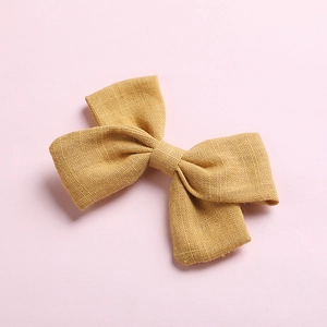Charming ginger yellow cotton bow hair clip with textured weave on a soft pink background