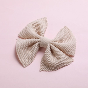 Detail of a large beige bow hair clip with textured honeycomb waffle fabric on pink background