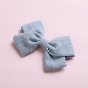 Detail of light blue cotton bow hair clip with textured fabric weave on pink background