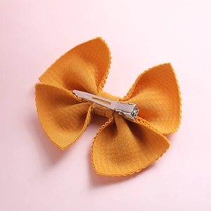 Close-up of ginger yellow bow hair clip with textured fabric and metal duckbill clip