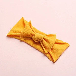 Detail of ginger yellow nylon baby headband featuring a large textured bow and soft hem