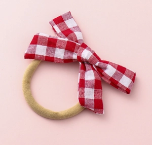 Detail of red and white checkered bow hair tie with high elastic band on pink background