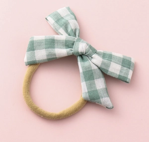 Detail of green and white plaid bow hair tie with high elastic nylon band on pink base