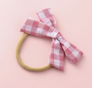 Detailed view of kids checkered pink and white bow elastic hair tie on a pink background