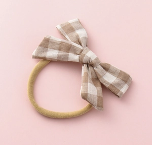 Close-up of baby headband with brown gingham bow on a stretchy khaki nylon band