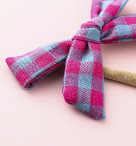 Macro view of checkered pink and blue bow hairband for infants with elastic nylon strap