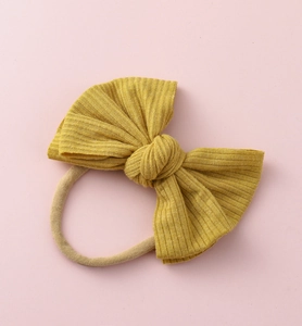 Détail d'un bandeau bébé en maille côtelée jaune moutarde avec nœud et ruban nylon