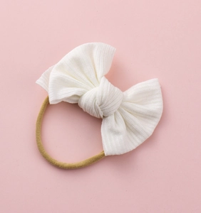 Détail du bandeau bébé avec nœud côtelé blanc attaché à un élastique en nylon de couleur chair