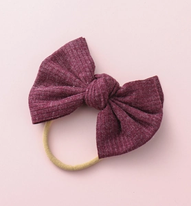Gros plan du bandeau bébé avec grand nœud en tissu côtelé bordeaux et ruban de nylon souple