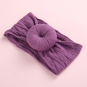 Purple cable knit baby headband with donut knot design on a soft pink background