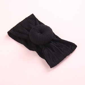 Elastic black cable knit baby headband featuring a stylish donut knot on a pink background