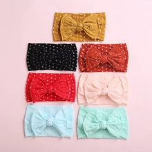 Flat lay of seven nylon baby headbands with large bows in assorted colors and polka dot patterns