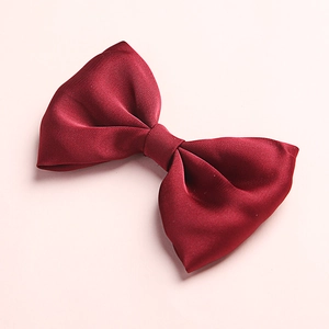Detailed view of a silky red satin bow hair clip for girls on a soft pink background