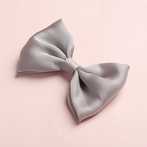 Detailed close-up of a grey satin fabric hair bow on a minimalist pink background