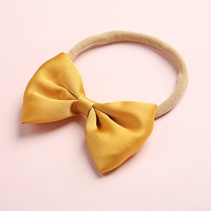 Close-up of golden satin bow headband with soft nude nylon elastic for baby girls
