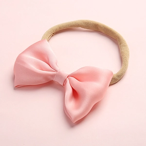 Detailed close-up of a large pink silk bow baby headband with elastic knit band