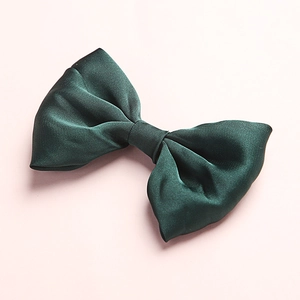 Detailed close-up of dark green satin bow hair clip on a soft pink background