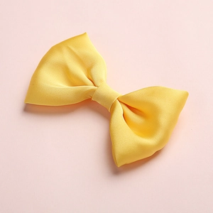 Close-up of a bright yellow satin bow hair clip with dense texture on pink background