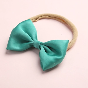 Detail of emerald green satin bow on soft beige nylon headband for infants and kids