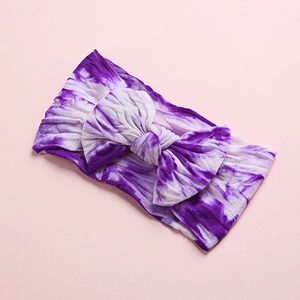 Close-up of purple tie-dye baby headband with a large soft knot bow on pink background